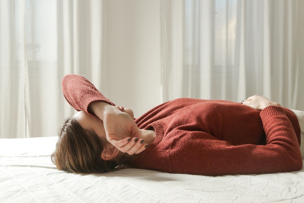 femeie culcata. reprezentand simptome dureroase ale dezechilibrului hormonal